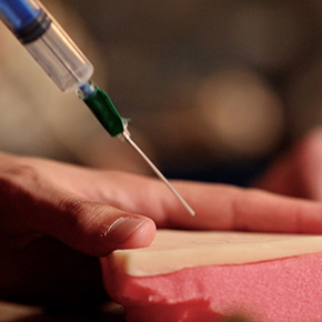 A hand inserts a syringe into a piece of equipment