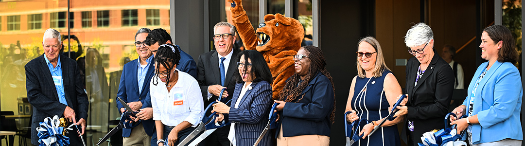 a group of people hold large scissors and cut a ribbon